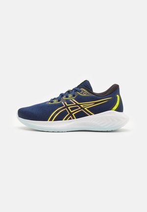 Scarpe sportive di colore blu scuro con parte superiore in rete, dettagli in neon giallo e suola bianca texturizzata. Presentano una punta arrotondata e un sistema di allacciatura per una calzata sicura.