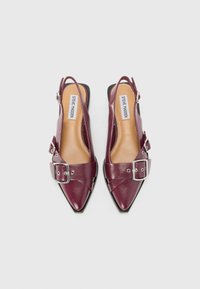 Burgundy leather slingback heels with pointed toes, wide strap and buckle detail, flat black soles, and smooth texture.