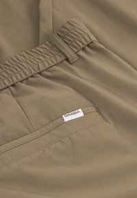 Khaki kalhoty s elastickým pasem, hladká textura a náprsní kapsa s bílou etiketou s nápisem "GABBA."