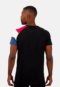 Zwarte t-shirt met een drielaags paneelontwerp met rode, witte en blauwe accenten op de schouder. Korte mouwen, casual pasvorm.