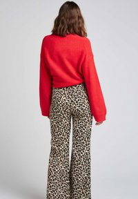 Pull rouge surdimensionné à manches longues associé à un pantalon évasé en imprimé léopard avec un fond clair et des taches foncées.
