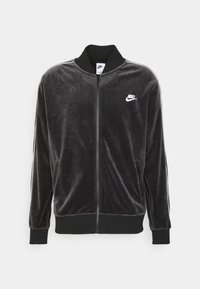  Černá sametová bunda na zip s vysokým stojacím límcem, bočními kapsami a bílým logem Nike na hrudi. Na rukávech jsou bílé pruhy.
