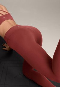 Bordový športový set pozostávajúci z priliehavého topu s tenkými ramienkami a legín s vysokým pásom, vyrobený z elastickej, hladkej tkaniny.