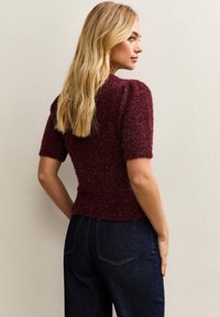 Burgundowa krótkosleeve sweter o teksturowanym, błyszczącym wykończeniu, dopasowany fason i ściągacz przy dekolcie, w połączeniu z ciemnoniebieskimi spodniami z wysokim stanem.