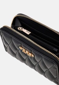 Black quilted leather wallet with gold zipper and Guess logo, open to show interior zippered pocket and card slots.