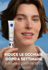 Trattamento per gli occhi NIVEA in un tubo bianco con dettagli dorati. Il modello ha i capelli corti e castani e sta tenendo il prodotto vicino al viso.
