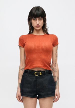 Κοντομάνικο μπλουζάκι σε σκουριά απόχρωση με ριμπ υφή, κοντά μανίκια και στρογγυλή λαιμόκοψη, συνδυασμένο με μαύρο τζιν σορτς και μαύρη ζώνη.