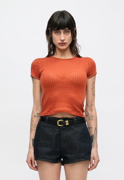 T-shirt court de couleur rouille avec une texture côtelée, manches courtes et col rond, associé à un short en denim noir et une ceinture noire.