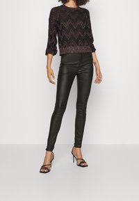 Svart, glittrig, stickad tröja med zigzag-mönster och tre fjärdedels ärmar, i kombination med tighta, blanka svarta byxor i konstläder och remmar av svarta klackar.