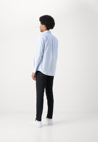 Lyseblå stribet skjorte med en buet kant, parret med sorte slim-fit bukser og hvide sneakers, set fra ryggen.