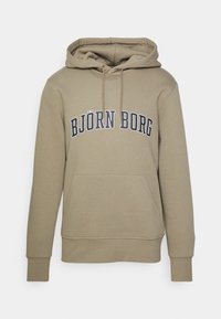 Mikina s kapucí v béžovém materiálu, s klokankovou kapsou, žebrovanými manžetami a potiskem loga tmavě modrou barvou na hrudi.