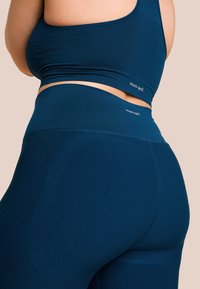 Marineblauw sportset bestaande uit een naadloze sportbeha en high-waisted leggings met geribbelde details en subtiele branding op de taille.