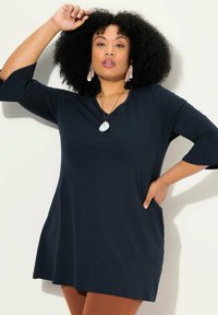 Marinblå tunika med trekvartslånga vid ärmar, avslappnad passform, rund halsringning och sidofickor, tillverkad av mjukt tyg.