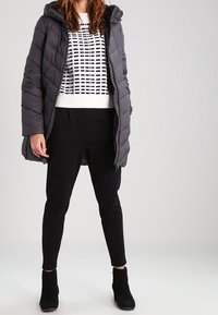 Padded gray parka with hood, quilted design, worn over a black and white patterned sweater, paired with black tapered pants and ankle boots.