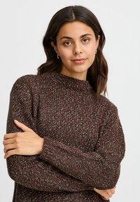 Suéter de punto marrón con un cuello alto, textura acanalada y motas de rojo y azul en todo su diseño. Mangas largas, corte relajado.