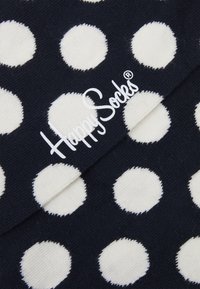 Calzini blu navy con grandi pois bianchi. Il tessuto appare morbido con una texture a maglia. Logo "Happy Socks" stampato in bianco.