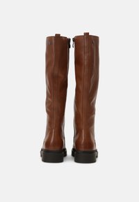 Bottes en cuir marron jusqu'au genou avec une texture lisse, fermeture éclair et semelle en caoutchouc noir. Des détails de couture sont visibles le long des côtés.