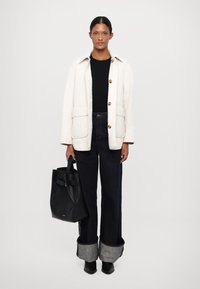 Cream quilted jacket with golden buttons, black top, dark denim wide-leg jeans with rolled cuffs, and a black leather tote bag.