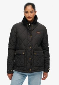 Sort quiltet jakke med en kordfløjlskrage, messingfarvede trykknapper, to frontlommer og en lynlås-lukning. Tekstureret stof, mellemlang design.