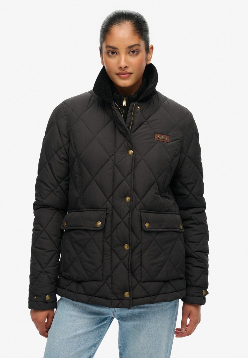 Sort quiltet jakke med en kordfløjlskrage, messingfarvede trykknapper, to frontlommer og en lynlås-lukning. Tekstureret stof, mellemlang design.