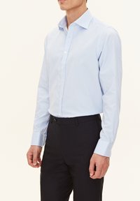 Camicia a righe azzurro chiaro con colletto button-down, maniche lunghe e design aderente, abbinata a pantaloni scuri.