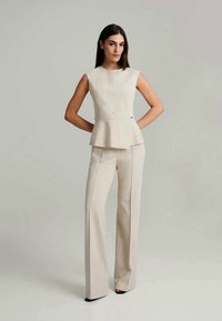 Beige peplum top med en let glans, parret med matchende højtaljede bukser. Glat stof, skræddersyet pasform og subtile silhuetdetaljer.