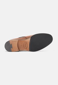 Hellbraunes Leder-Schuhwerk mit glatter Oberfläche, ausgestattet mit einer strukturierten schwarzen Gummisohle und einem hellbraunen Leder-Fersenakzent. Branding ist auf der Sohle sichtbar.