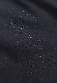 Gotas de agua formando perlas sobre una tela impermeable negra, mostrando su resistencia al agua y textura.