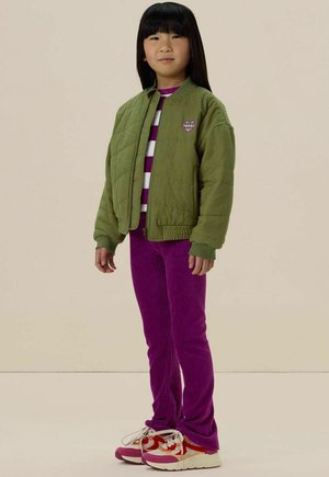 Veste bomber matelassée verte avec des poignets côtelés, chemise rayée blanche et violette, pantalon en velours côtelé violet et baskets rouges et blanches.