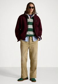 Μπορντό μπουφάν, πράσινη και γκρι ριγέ πόλο, ανοιχτό μπλε πουκάμισο, μπεζ παντελόνι άνετης εφαρμογής, πράσινα παπούτσια. Σημαντικές λεπτομέρειες: γυαλιά ηλίου και παντελόνι με μπαλώματα.