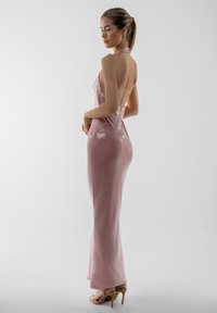 Uskačajući ružičasti haljina s šljokicama, halter dekolteom, bez leđa i teksturiranom površinom; kombinirana s golim štiklama.