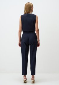 Une combinaison sans manches bleu marine avec un corsage ajusté et un pantalon fuselé, présentant une texture lisse et un design minimaliste.