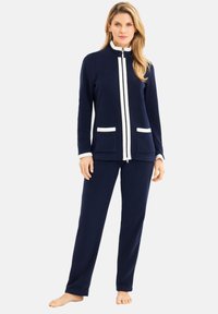Marineblaue Fleece-Loungewear bestehend aus einer Reißverschlussjacke mit weißen Akzenten und zwei Vordertaschen, kombiniert mit passenden Hosen.