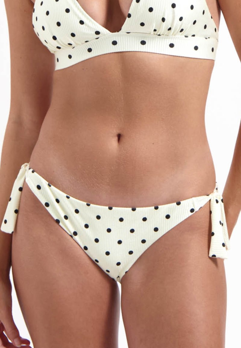 Set bikini a pois in crema con punti neri. Tessuto a coste. Il top presenta un design triangolare; il fondo ha lacci laterali e un taglio basso.