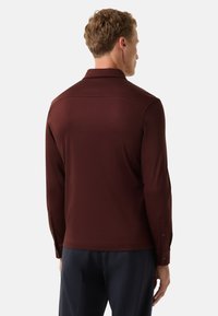 Bordeauxfarbiges Langarmhemd mit elegantem Design, das einen Kragen, geknöpfte Manschetten und eine glatte Textur aufweist.