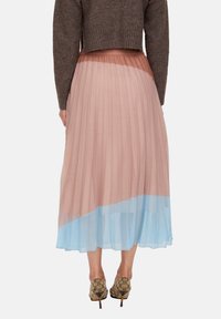 Pleated midi skirt in soft pink and pale blue, featuring a translucent finish. Paired with a cropped brown knit sweater and patterned heels.