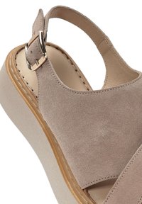 Sandal in camoscio beige con tallone aperto, cinturino regolabile con fibbia e suola a piattaforma strutturata in beige chiaro. Dettagli di cucitura lungo i bordi.