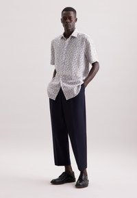 Korte mouwen, gemusterd shirt in het wit met een multikleurige bloemenprint, gecombineerd met donkerblauwe, wijde broek en zwarte veterschoenen.