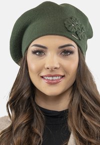 Zelená pletená beretka s texturovaným povrchem, která je zdobena třemi látkovými květinami a malým kovovým akcentem na boku.