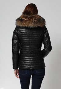 Chaqueta de cuero negra con una textura acolchada y un gran cuello forrado de piel. Ajuste entallado que acentúa la forma. Vista trasera que resalta los detalles de la costura.