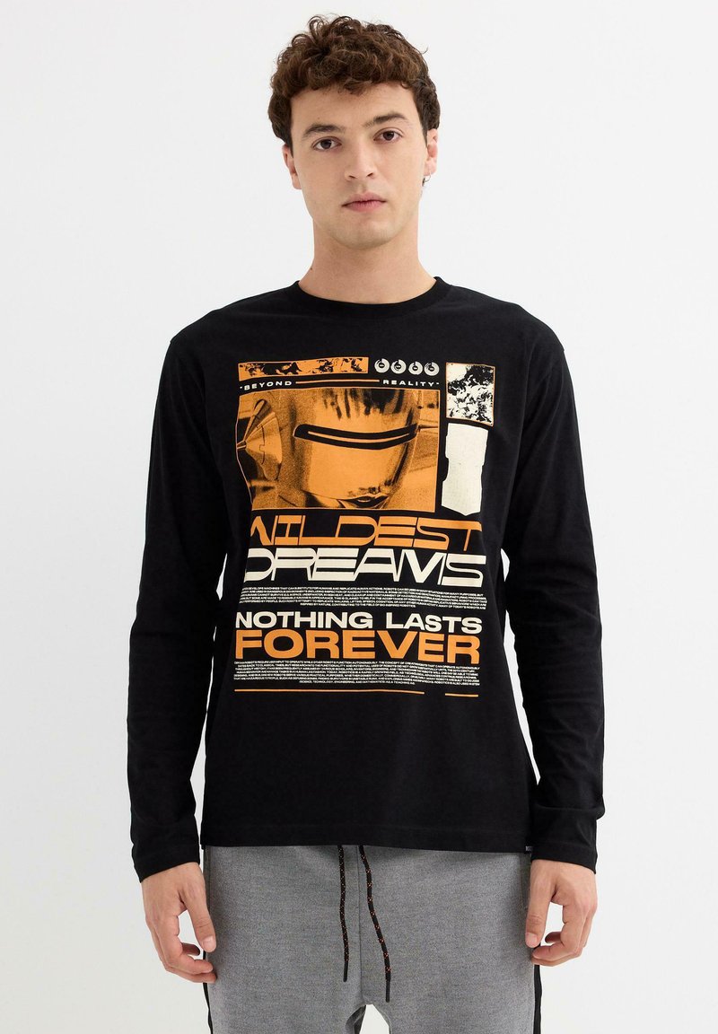 Joven vistiendo una camiseta de manga larga negra con el texto en naranja y blanco "Wildest Dreams Nothing Lasts Forever" y un diseño gráfico en el frente.