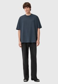 Oversized blue cotton t-shirt with a crew neckline and short sleeves, paired with black straight-leg jeans and black shoes with metallic accents.
