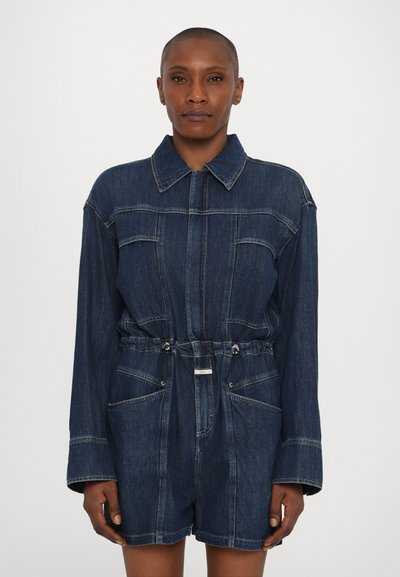 Denim jumpsuit i mørkeblå med lange ærmer, kravehalsudskæring og elastisk talje. Har to forlommer og synlige stikninger.