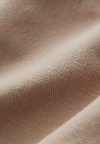 Beige vævet stof med en glat tekstur, der udviser et fint, ensartet mønster og en subtil glans, som hænger blødt i forskellige folder.