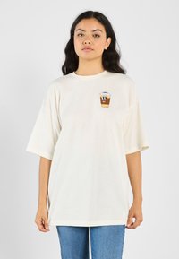 Krämfärgad oversized t-shirt med korta ärmar som har en tecknad kaffekopp på bröstet. Mjuk bomulls material, avslappnad passform.