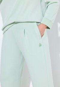 Mintgroene joggingsbroek van zacht materiaal, met zijzakken, een geribbelde enkelmanchet en een klein geborduurd logo op de dij.