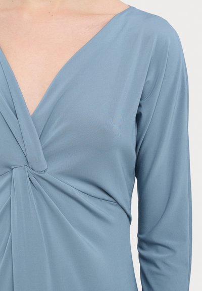 Zacht blauwe jurk met lange mouwen en een diepe V-hals. Heeft een gedraaide detail bij de taille en een soepel, rekbaar materiaal.