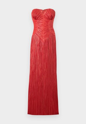 Frau trägt ein trägerloses, bodenlanges rotes plissiertes Kleid mit tailliertem Oberteil, kombiniert mit schwarzen Sandalen mit hohen Absätzen vor einem schlichten Hintergrund.