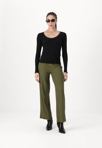 Top negru cu dungi, cu mâneci lungi și detalii din dantelă; pantaloni evazați din rib normaal, de culoare verde măslinie; cizme negre cu vârf ascuțit până la gleznă; ochelari de soare supradimensionați.
