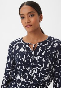 Robe marine avec un motif abstrait blanc, encolure ronde et une ouverture en forme de clé à l'avant. Manches longues avec une coupe décontractée.